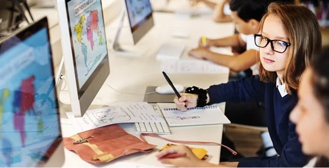 School-age girl with glasses working on computer with colorful charts and data visualization projects in classroom