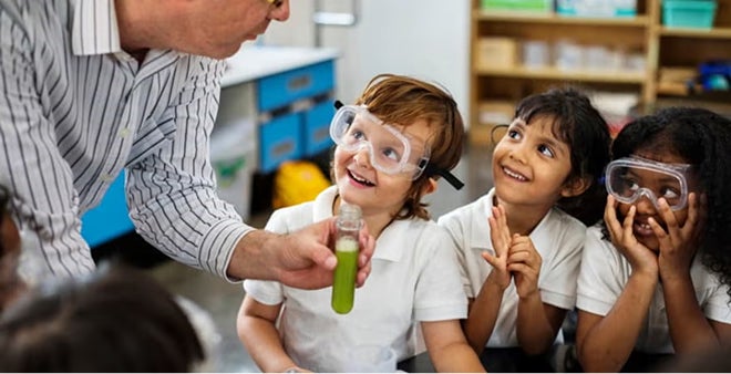 Teacher conducting science experiment with children wearing safety goggles