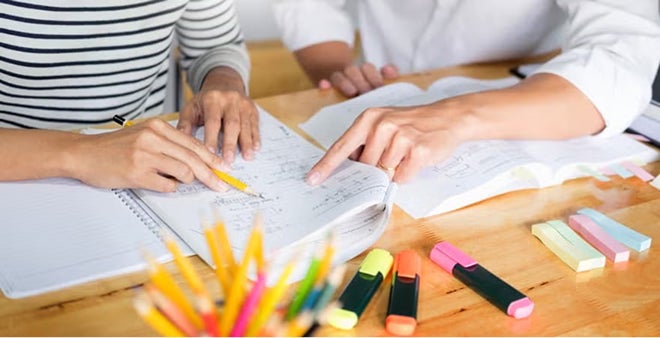 Close-up of students studying together with notebooks, colored pens, and highlighters on wooden desk