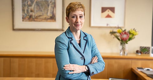 A woman in a blue suit and tie stands confidently in front of a desk, exuding professionalism and authority.