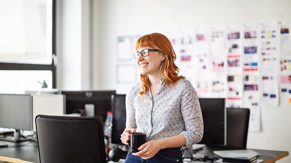 A woman wearing glasses stands in front of a computer, focused on the screen.