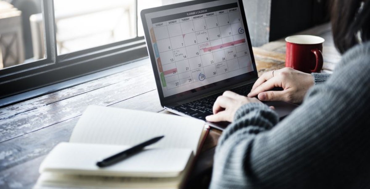 An ECU Online Student is sitting at a desk. We can see their notebook and laptop screen which has a weekly planner open.