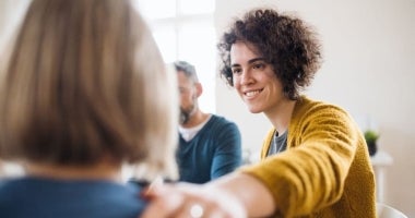 An ECU Master of Counselling student is sitting facing another person. She has her hand on their shoulder and is smiling at them.